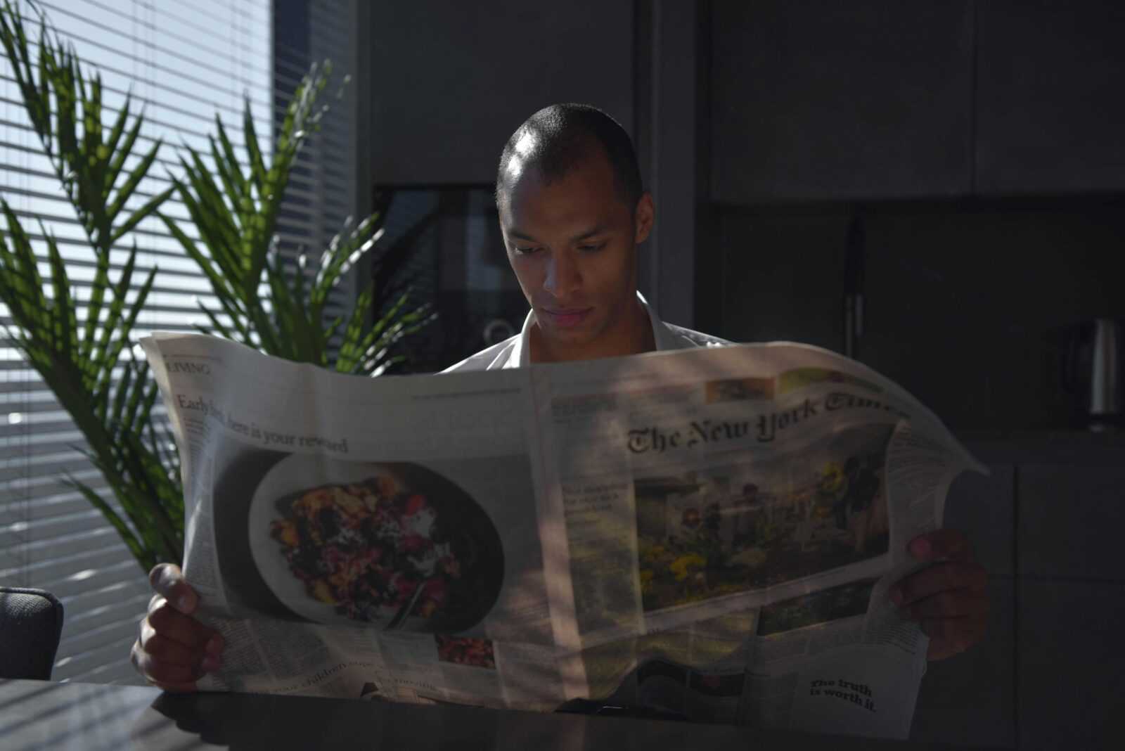 Businessman focused on reading newspaper in a sunny indoor office setting.